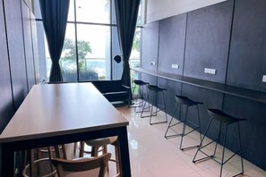 A modern room with a long table, several bar stools, and a view through large windows.