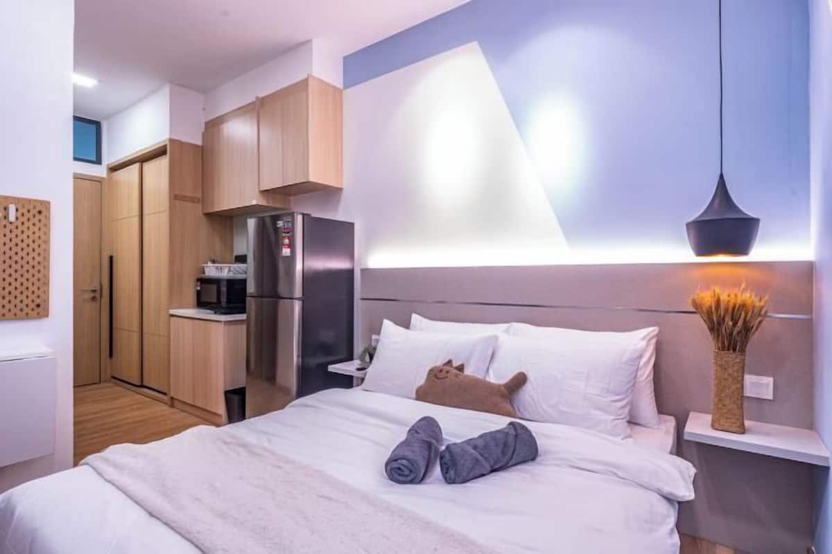 Een moderne hotelkamer met een bed, een kleine kitchenette en een wandplank met een vaas.
