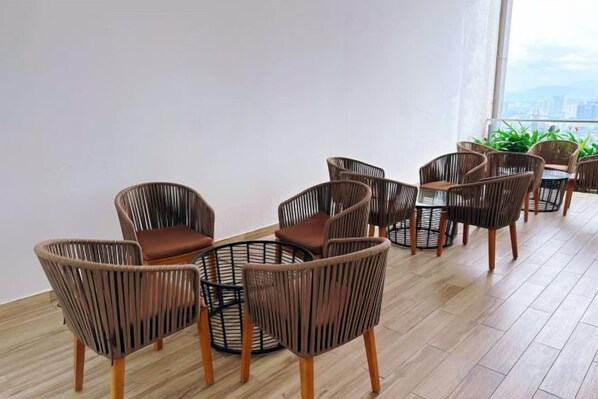 A room with wicker chairs and a table, large windows, and a view of the city.