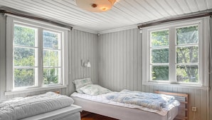 Een kleine eenpersoonskamer met twee bedden, grote ramen, houten vloeren en een wit plafond.