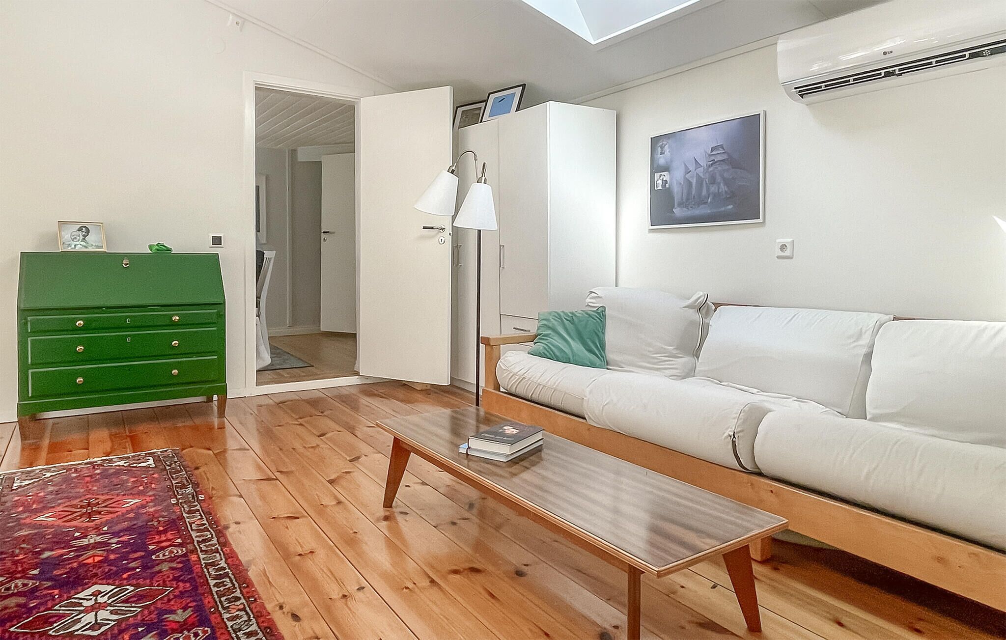 Una sala de estar con un sofá blanco, un aparador verde, una mesa de centro de madera y una alfombra estampada.