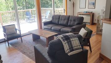 Ein Wohnzimmer mit einer Couch, Sesseln, einem Couchtisch und Blick durch eine Glastür auf eine Terrasse.
