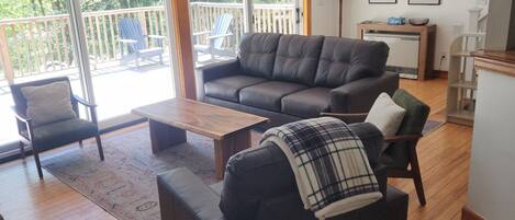 A living room with a sofa, armchairs, a coffee table, and a view through a sliding glass door to a deck.