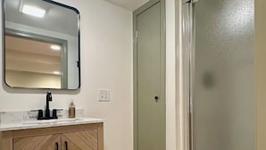 Ein Badezimmer mit einem Holzkosmetikschrank, einem Spiegel und einer Milchglas-Tür.