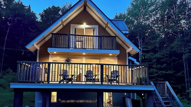 Eine zweistöckige Holzhütte mit Balkon, Treppe und einer Terrassenfläche.