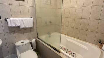 Un baño moderno con ducha envuelta en vidrio, inodoro blanco y bañera con felpudo de motivos florales.