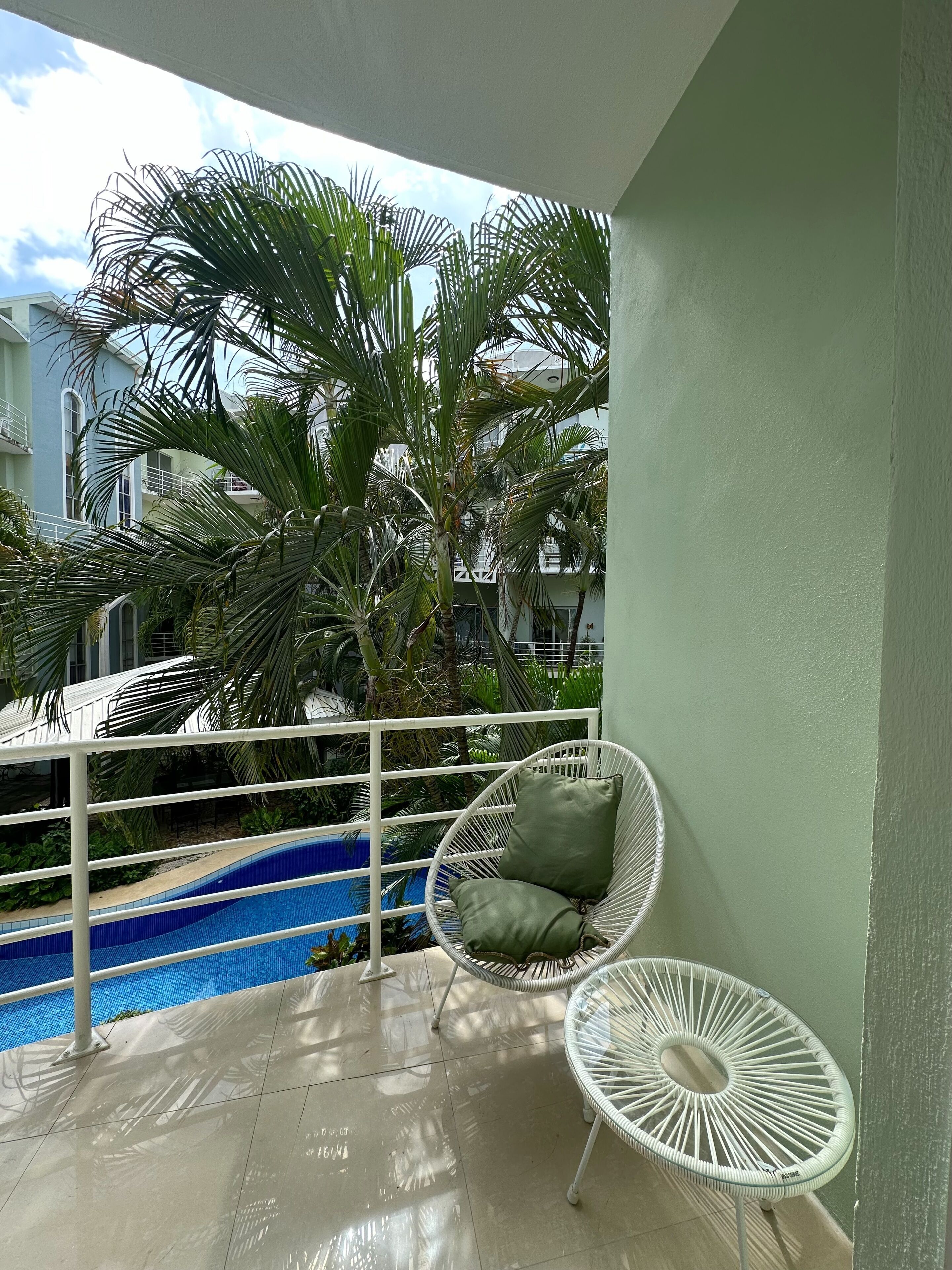 Un balcón con piscina, una silla blanca con cojines y otra silla blanca con un cojín.