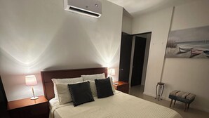 Een slaapkamer met een groot bed, twee nachtkastjes met lampen, een plafondventilator, een airconditioning en een schilderij aan de muur.