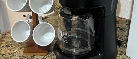 A coffee maker on a granite countertop with a mug holder to the left.