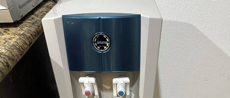 Um dispensador de água com dois bicos, um para água quente e outro para água fria, e um painel de controle com o logotipo da marca.