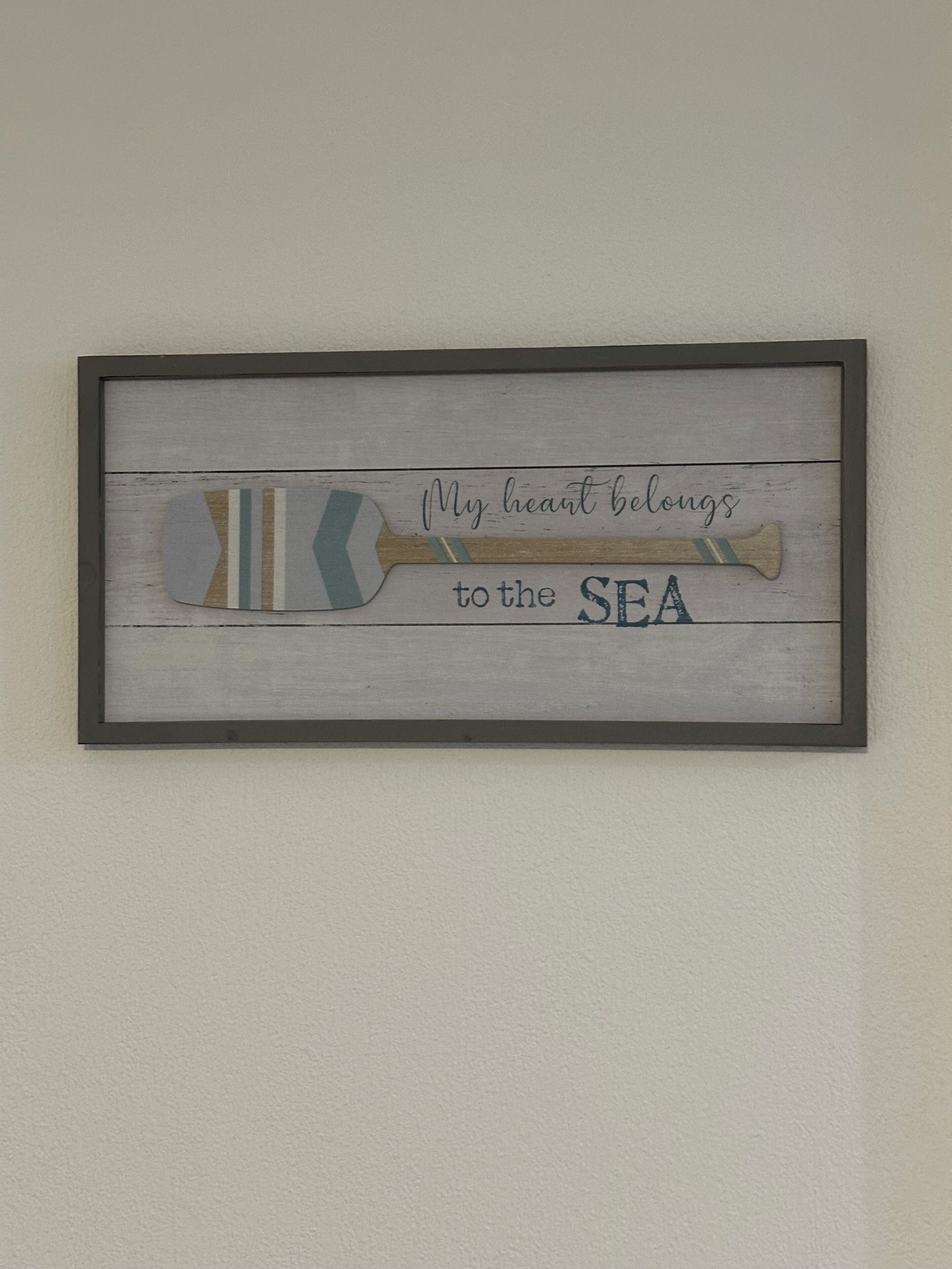 Una obra de arte náutica enmarcada con el texto 'My heart belongs to the SEA' en una pared.