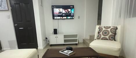 Un salon avec un téléviseur fixé au mur, un canapé, une table basse et un meuble.