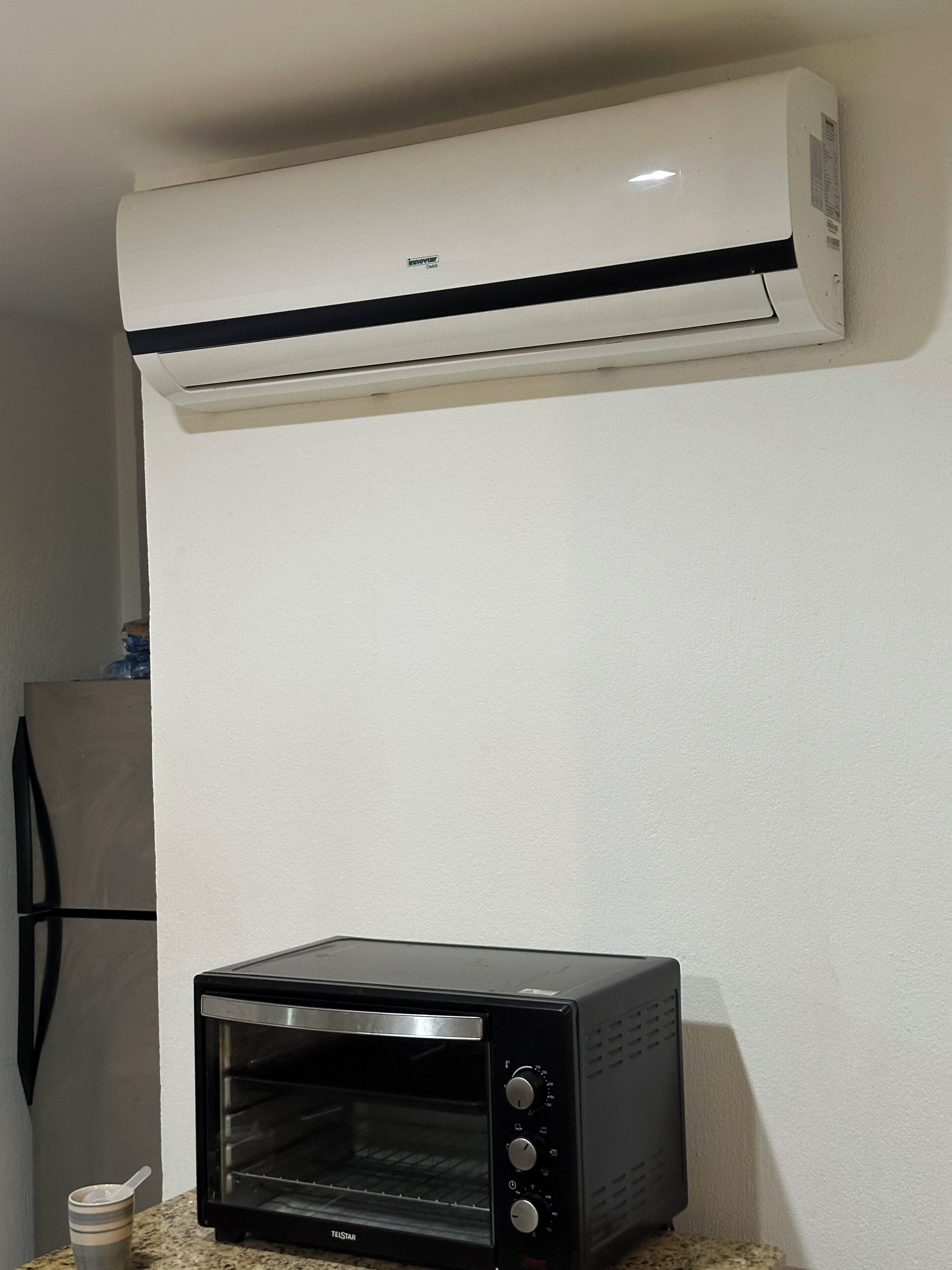 Una cocina con un horno tostador negro y un aire acondicionado blanco instalado en la pared.