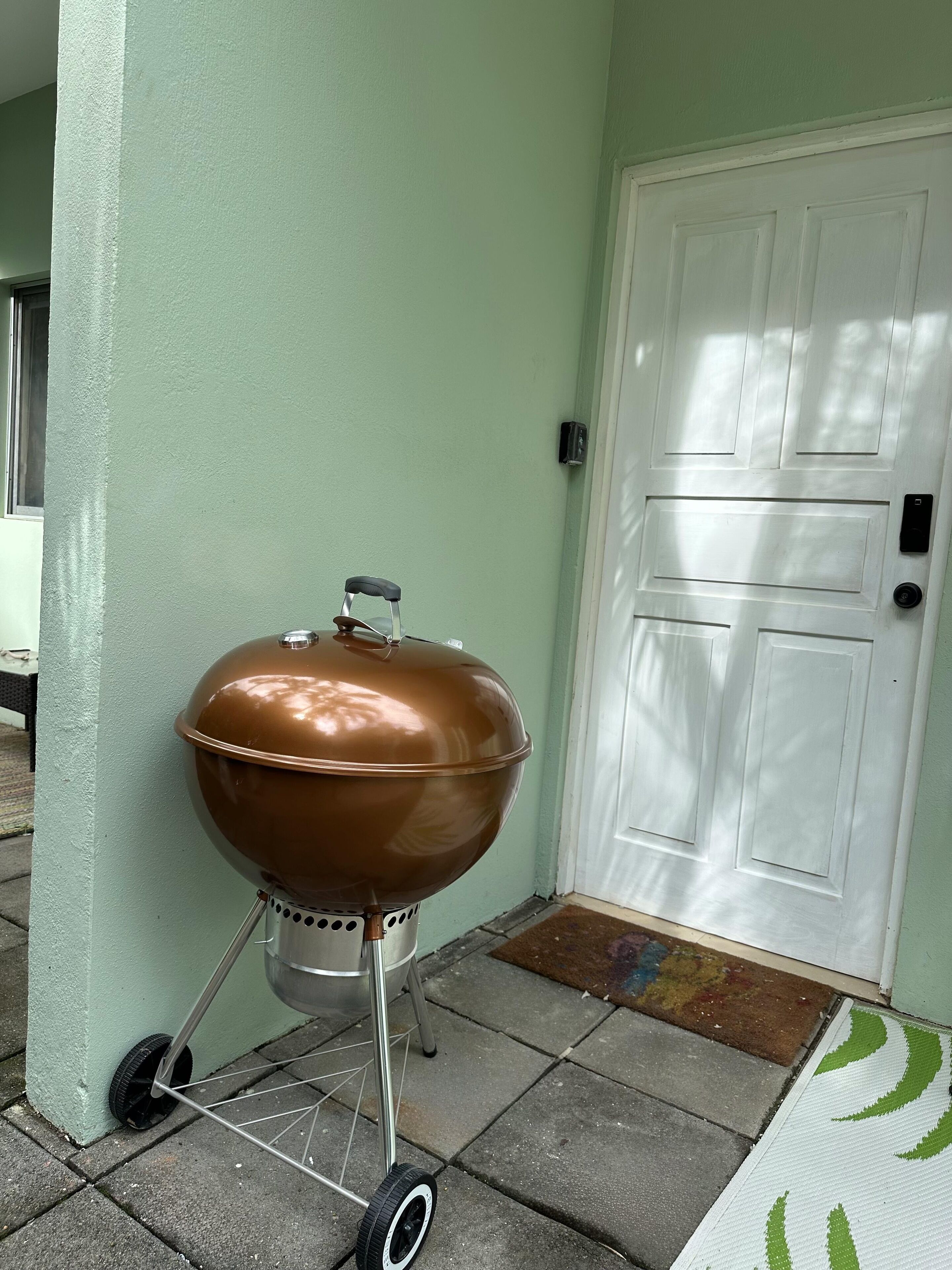 Un barbecue portable, placé contre un mur avec une porte blanche et un paillasson.