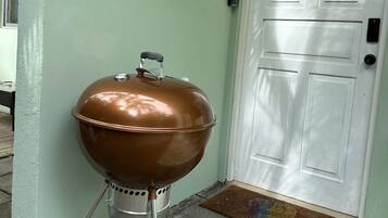 Un barbecue portable, placé contre un mur avec une porte blanche et un paillasson.