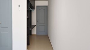 Um corredor estreito com uma porta cinzenta no final, um cabideiro e uma estante na parede.