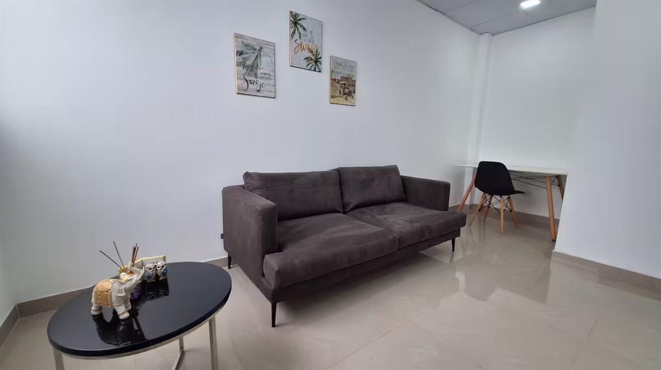 A modern living room with a grey sofa, a small black table, and a black chair. There are three framed pictures on the wall.