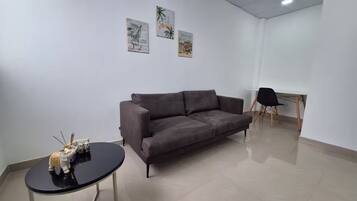 A modern living room with a grey sofa, a small black table, and a black chair. There are three framed pictures on the wall.