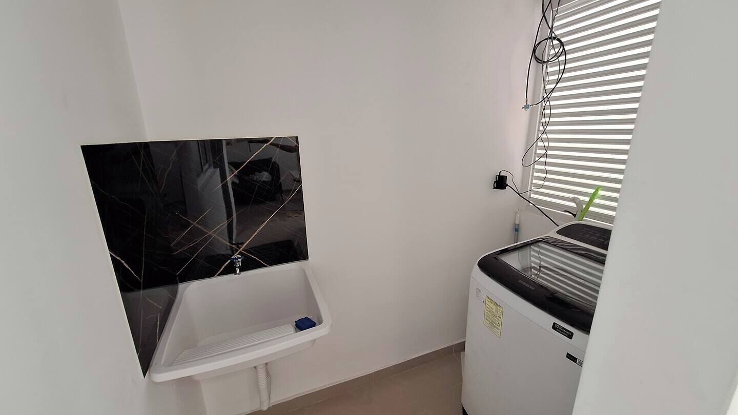 Een kleine badkamer met een wit wastafelmeubel, een zwart betegelde onderkast en een witte wasmachine.