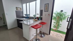 Una cucina moderna con isola centrale, sgabelli rossi, un frullatore e una pianta in vaso.