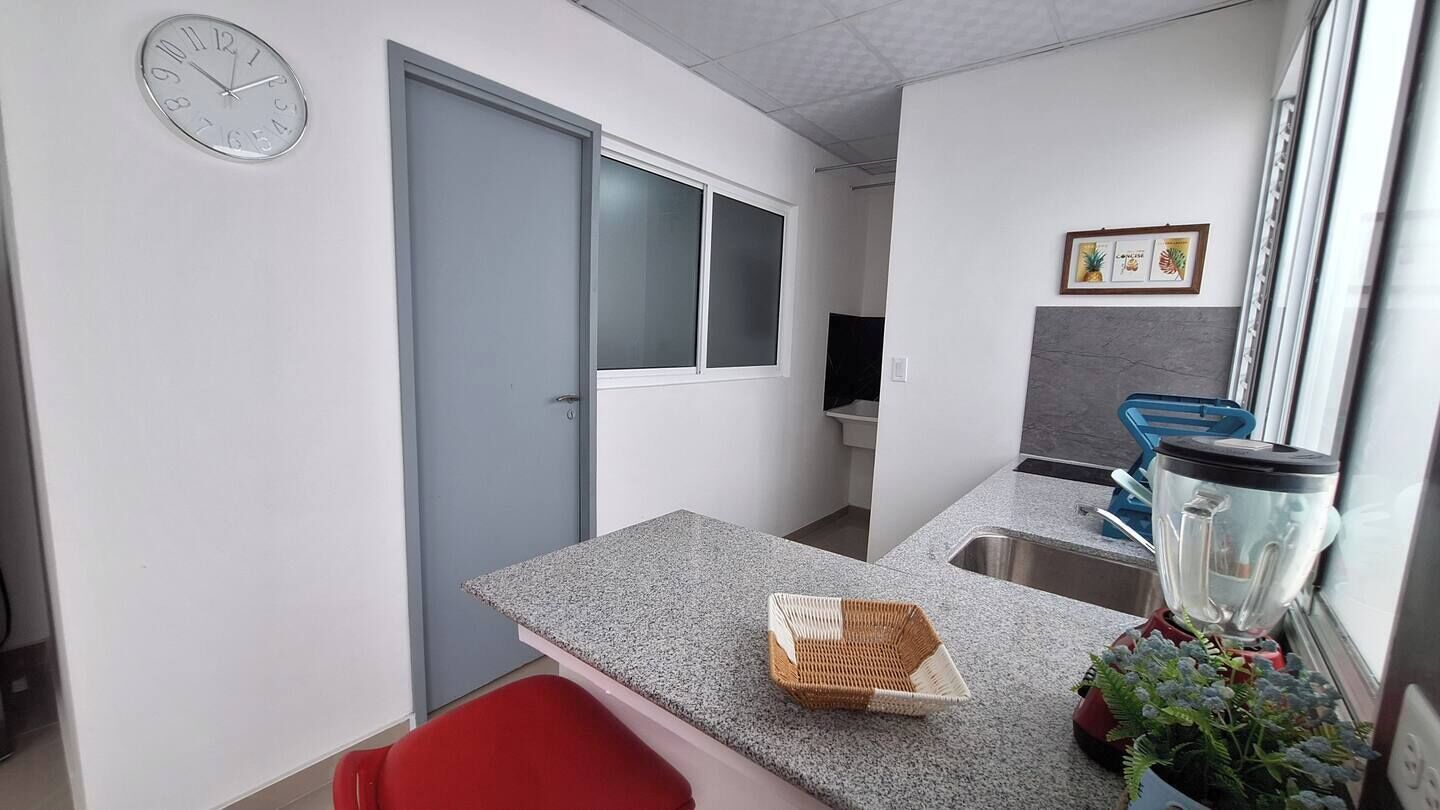 A compact kitchen with a granite countertop, a wicker basket, and a red chair.