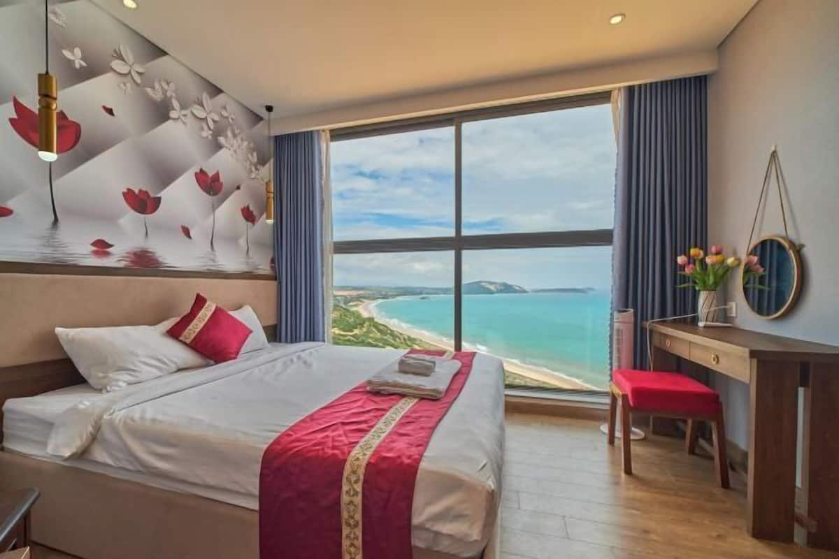 Une chambre d’hôtel avec un grand lit, un bureau et une vue sur la plage.