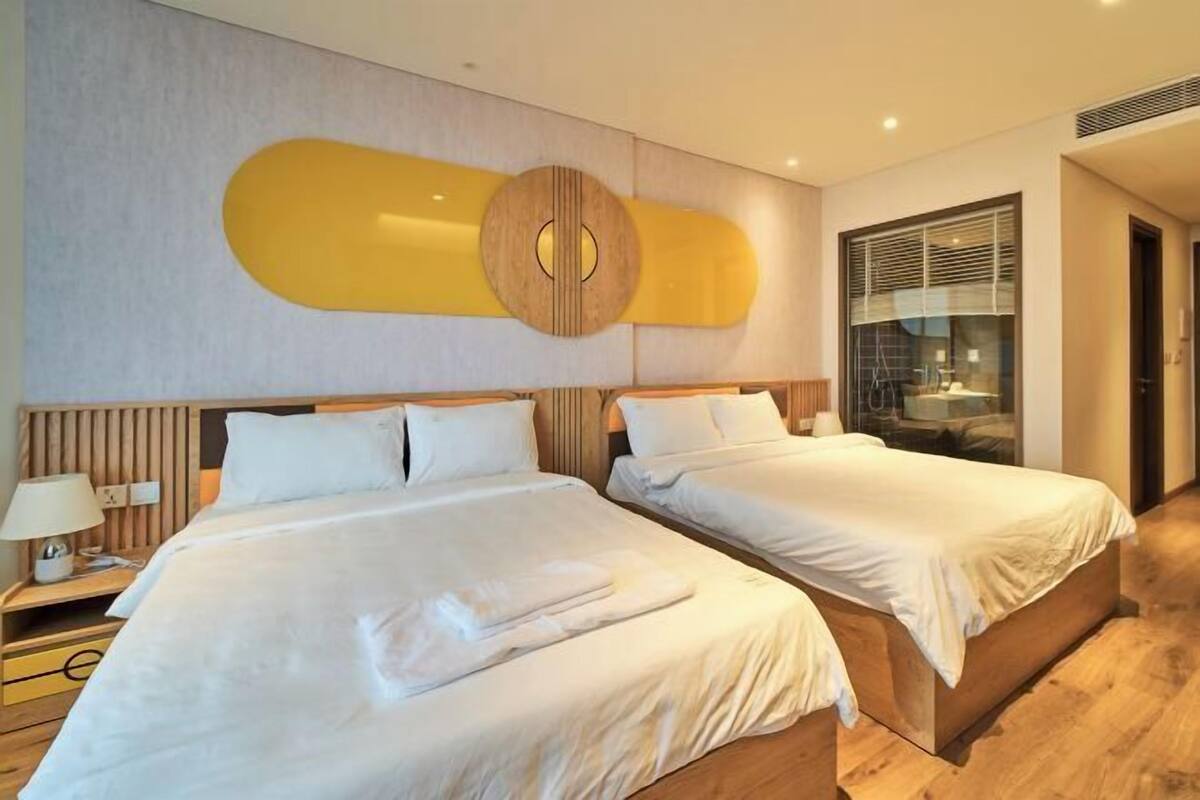 Une chambre d’hôtel avec deux lits, une tête de lit en bois, un grand miroir et une fenêtre avec des stores.