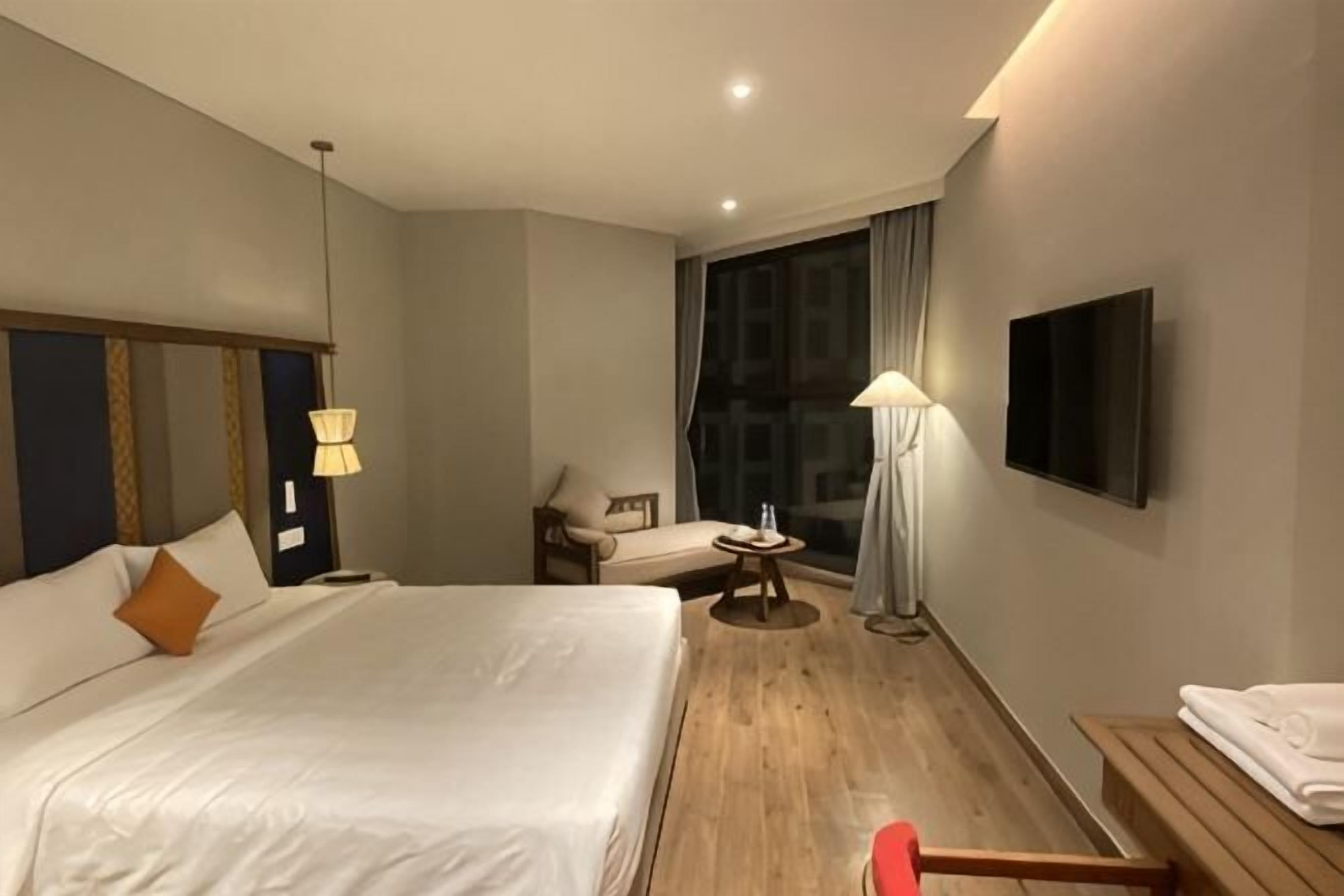 A hotel room with a large bed, a desk, a chair, a TV, and a window.