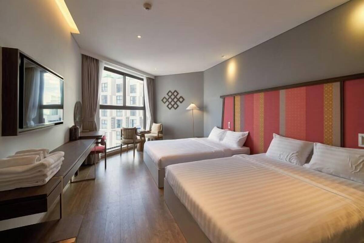 Une chambre d’hôtel avec deux lits, un bureau, une chaise et une grande fenêtre.