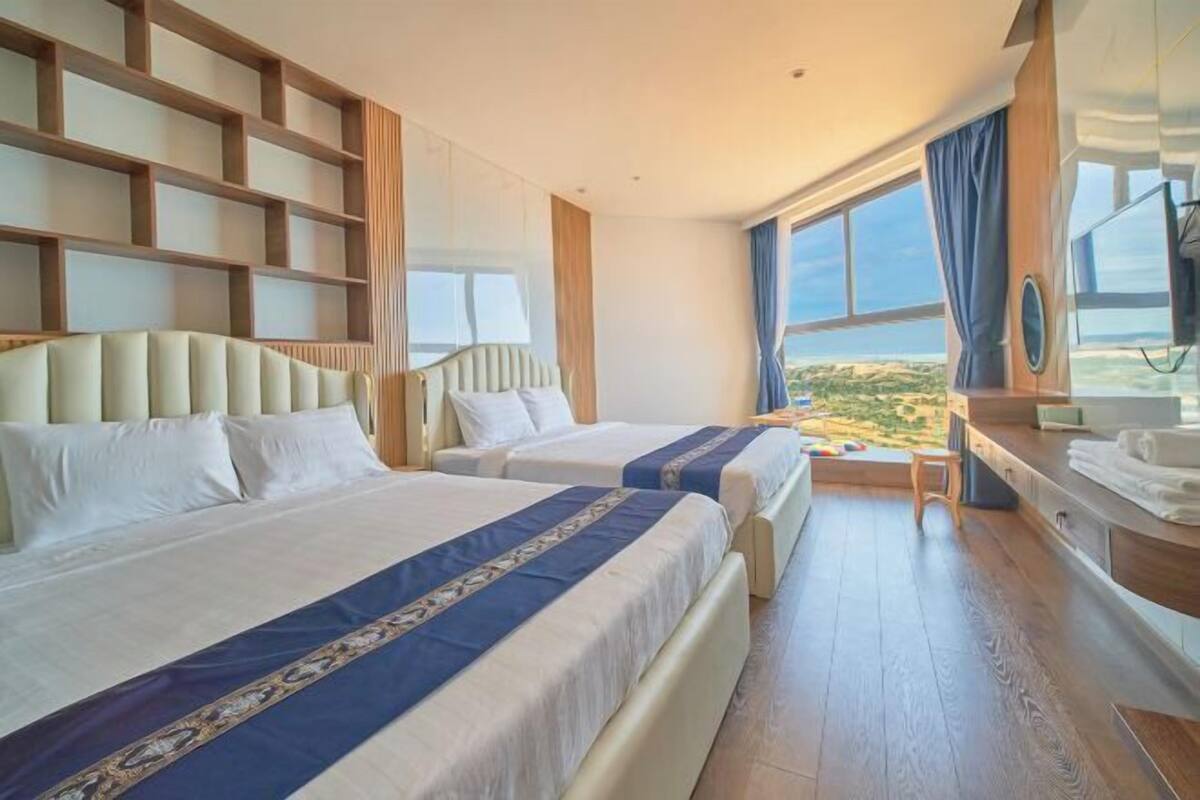 Une chambre d’hôtel avec deux lits, un bureau, une télévision et une grande fenêtre donnant sur un beau paysage.