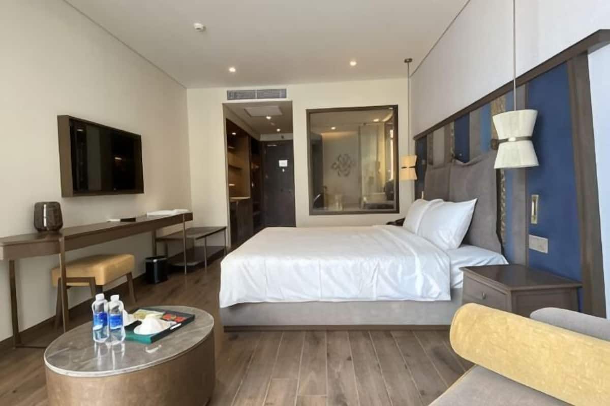 Ein Hotelzimmer mit Bett, Schreibtisch, Stuhl, rundem Couchtisch und Fernseher.