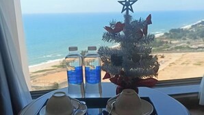 Une table avec deux tasses et deux bouteilles d’eau, un petit sapin de Noël, et une vue sur la plage et l’océan par une fenêtre.