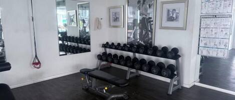 A gym with a bench, dumbbells, and a mirror.