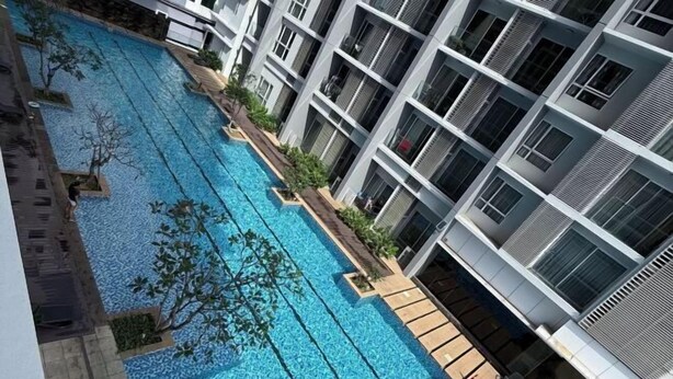 Un bâtiment moderne doté d’une piscine, entouré de verdure et caractérisé par une structure à plusieurs étages avec des balcons.