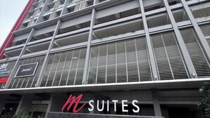 Un hôtel à plusieurs étages doté d’une architecture moderne, avec une enseigne « M SUITES » bien visible au niveau du rez-de-chaussée.