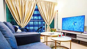 A modern living room with a sofa, two round tables, a flat-screen TV, and a view of a building through large windows.