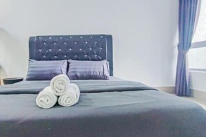 A neatly made bed with a tufted headboard, two pillows, and rolled towels.