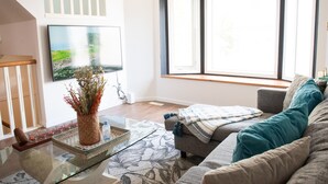 A living room with a sofa, a glass coffee table, a decorative vase, and a television mounted on the wall. - Central 3BR Getaway/ Family-sized, Free Parking & AC/ Near Downtown (Edmonton)
