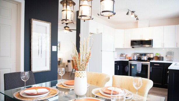 A modern dining area with a glass table, orange plates, and a vase with dried plants. - Central 3BR Getaway/ Family-sized, Free Parking & AC/ Near Downtown (Edmonton)