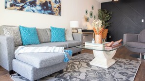 A modern living room with a grey sofa, a glass coffee table, and a ceiling fan. - Central 3BR Getaway/ Family-sized, Free Parking & AC/ Near Downtown (Edmonton)