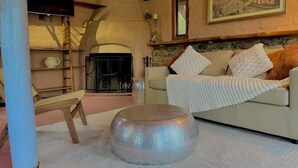 A cozy living room with a fireplace, a sofa with cushions, a round table, and a painting on the wall. - Maccy's Cottages (Macclesfield)