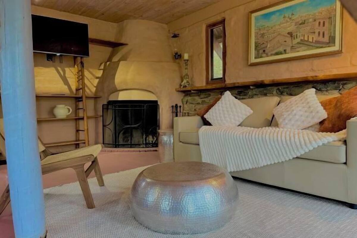 A cozy living room with a fireplace, a sofa with cushions, a round table, and a painting on the wall.
