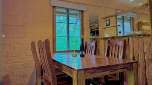 A wooden dining table with chairs, a window with blinds, and a kitchen area in the background. - Maccy's Cottages (Macclesfield)