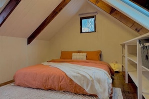 A bedroom with a sloped ceiling, a bed with orange bedding, a small window, and built-in shelving. - Maccy's Cottages (Macclesfield)