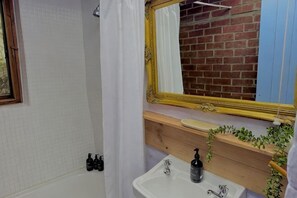 Une salle de bain avec un lavabo blanc, un miroir avec un cadre doré et un rideau de douche.