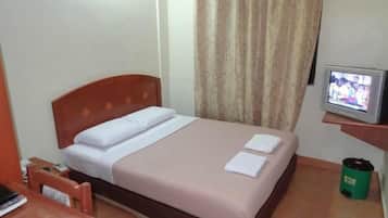 Una habitación de hotel con una cama, un televisor sobre un mueble, un bote de basura verde y una mesita de noche de madera.