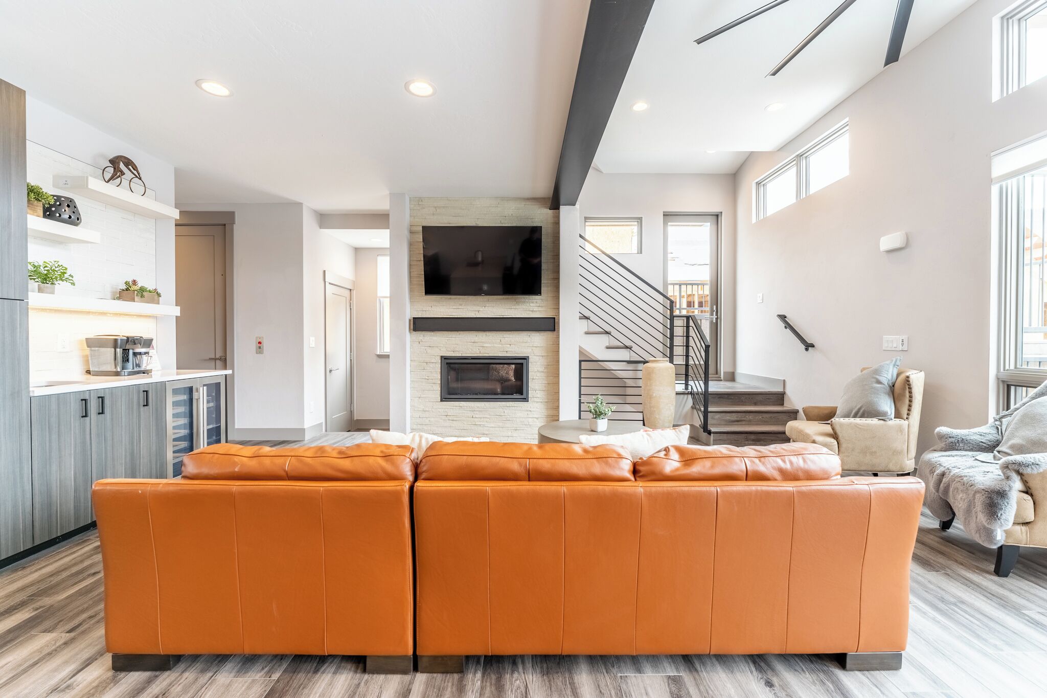 A modern living room with a large orange sectional sofa, a fireplace, and a staircase leading to another level.