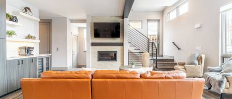 A modern living room with a large orange sectional sofa, a fireplace, and a staircase leading to another level.