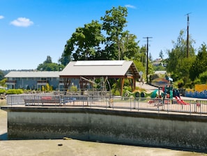 A playground with swings and slides, a covered pavilion, and a building with a flat roof in the background.