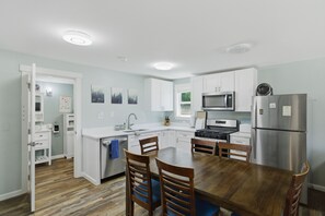 A modern kitchen with white cabinetry, a wooden dining table, and a stainless steel refrigerator.